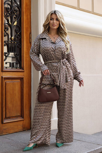 A woman models a brown and beige houndstooth patterned matching set consisting of a long-sleeve collared shirt and wide-leg trousers, styled with a brown handbag and green heels.