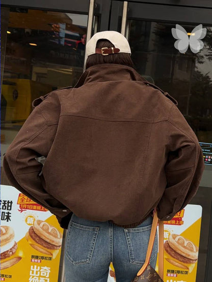 A person viewed from behind wearing a brown oversized jacket, blue jeans, and a cream baseball cap, standing in front of a storefront with yellow promotional posters.