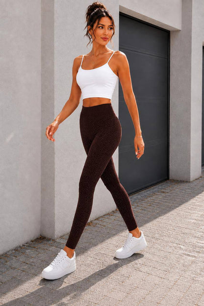 A woman modeling a matching activewear set consisting of a white spaghetti-strap crop top and dark brown textured leggings, paired with white sneakers, walking outdoors against a modern concrete wall and dark garage door.