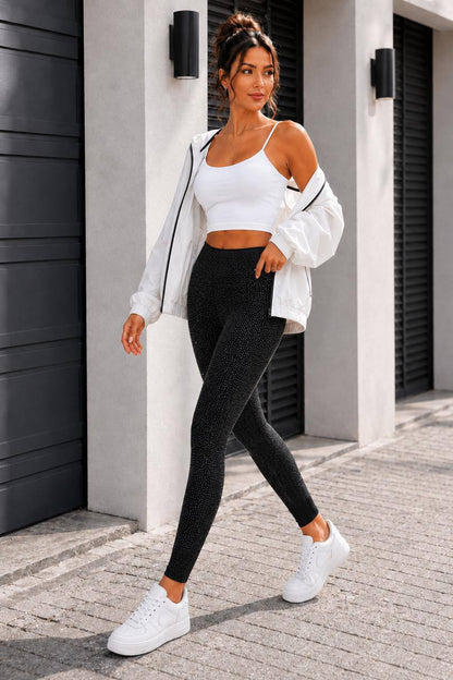 A woman modeling an athletic outfit consisting of a white crop top, black textured leggings, a white zip-up jacket, and white sneakers, standing outdoors in front of a modern building wall.