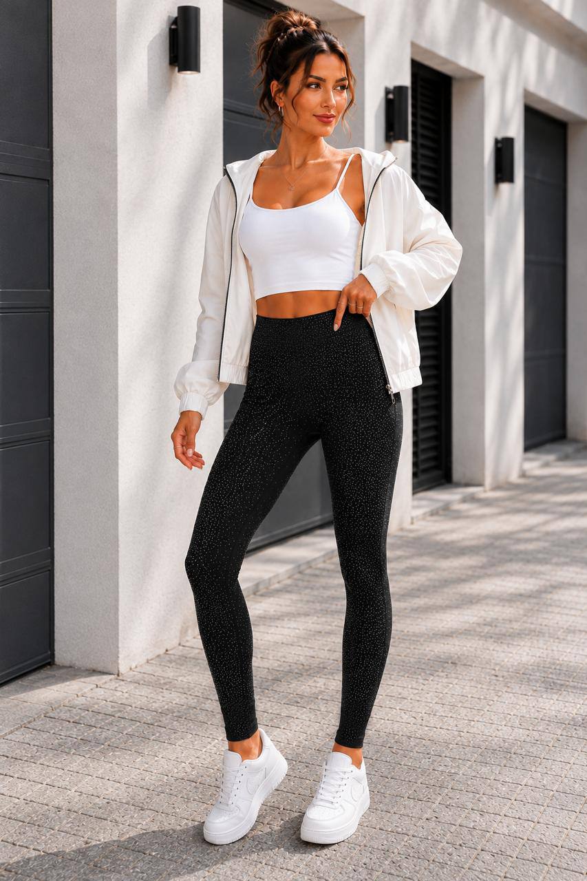 A woman stands outdoors wearing a white sports bra, black patterned leggings, a white zip-up hoodie, and white sneakers.