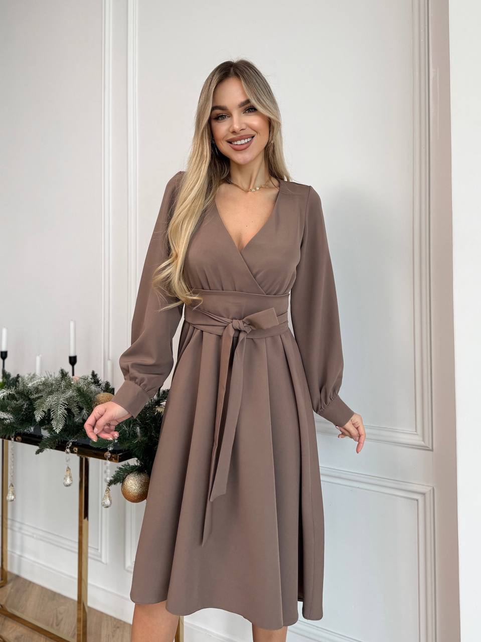 Woman wearing a brown dress standing in a room with decorative elements.