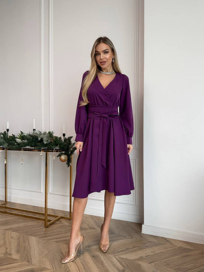 Woman wearing a purple dress standing in a room with a decorative table in the background.