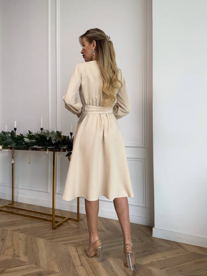 Woman in a beige dress standing in a room with a decorative table and candles.