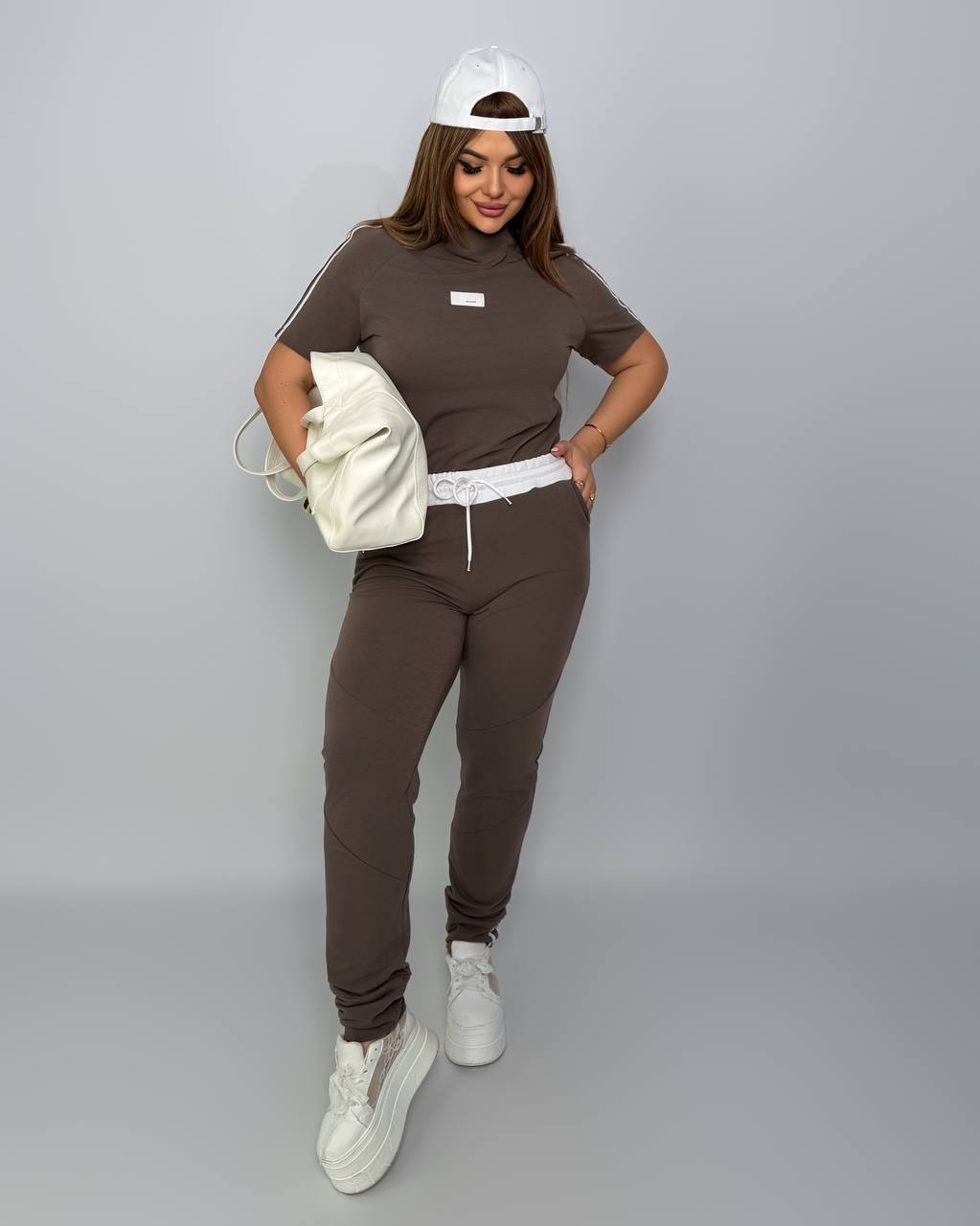 Person wearing a brown outfit with white sneakers on a gray background