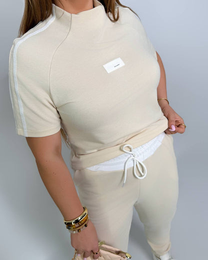 Person wearing a beige outfit with white accents on a plain background