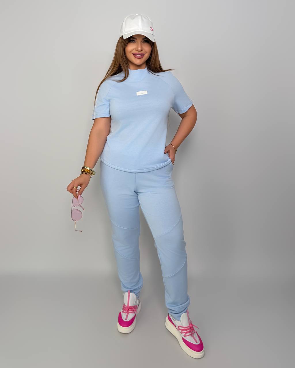 Woman wearing a light blue outfit with a white cap on a gray background