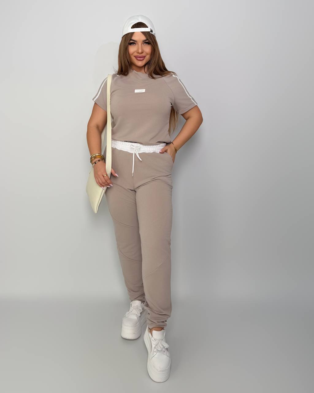 Woman wearing a beige tracksuit with white sneakers on a gray background