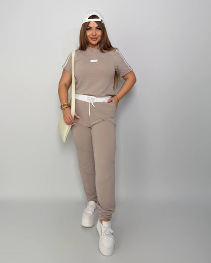 Woman wearing a beige tracksuit with white sneakers on a gray background