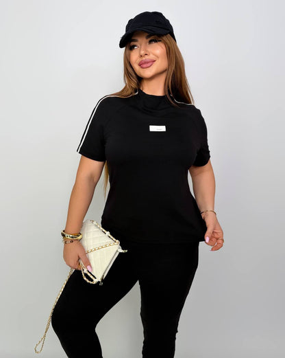 Woman wearing a black outfit with a white stripe and holding a small white handbag on a plain background