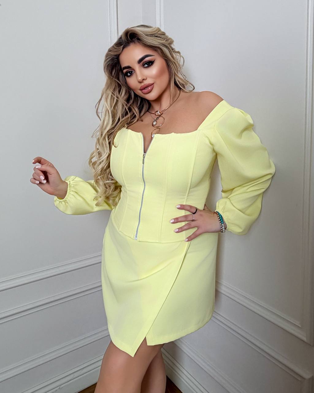 Woman wearing a light yellow dress against a white wall