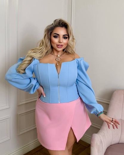 Woman wearing a blue off-shoulder top and pink skirt against a neutral wall.