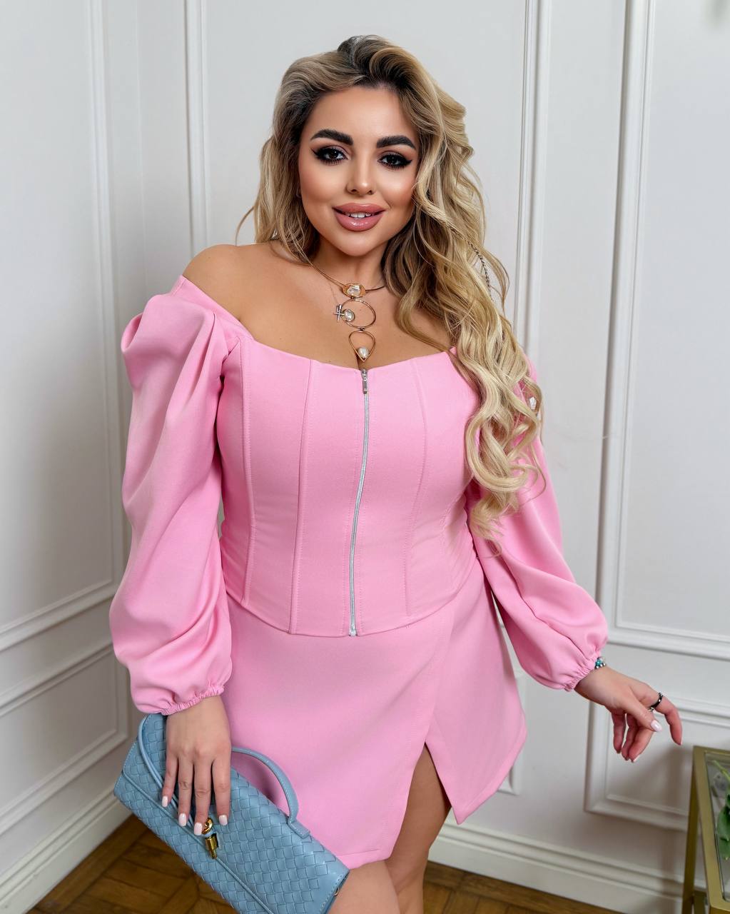 Woman wearing a pink off-shoulder dress with balloon sleeves against a white wall.