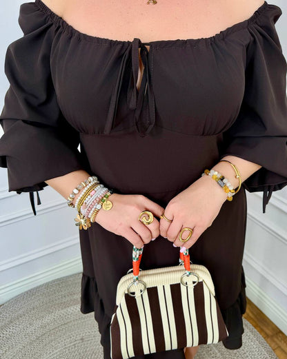 Person wearing a black off-shoulder top and holding a striped handbag.