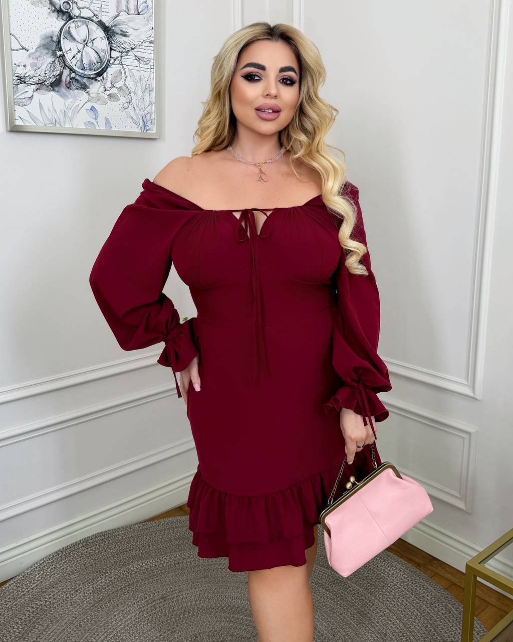 Woman in a burgundy dress holding a pink clutch in an elegant room.