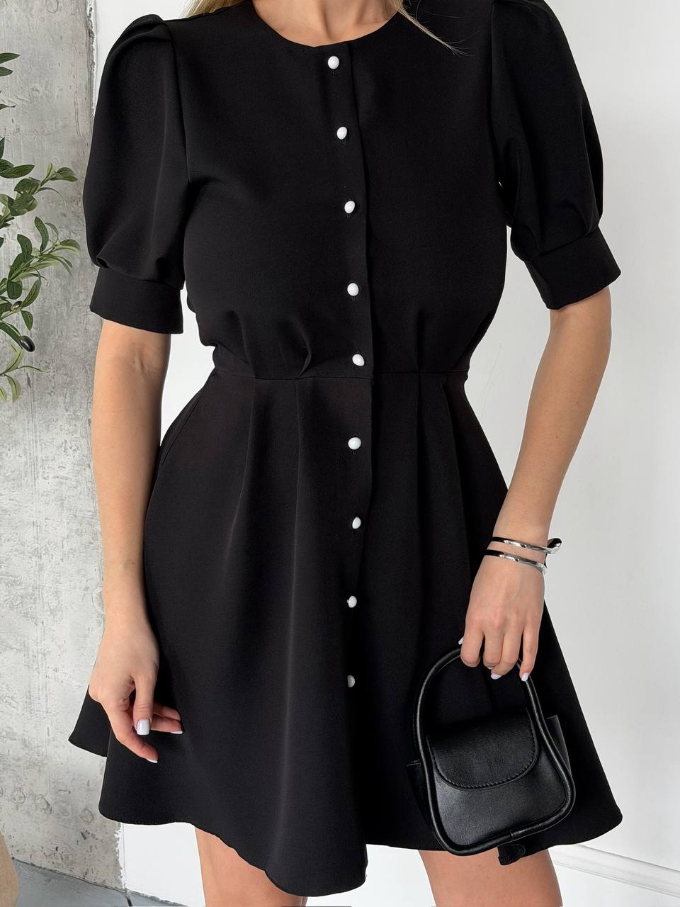 Black dress with white buttons worn by a person against a light background