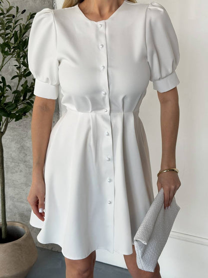 White dress with puff sleeves worn by a person, standing against a neutral background.