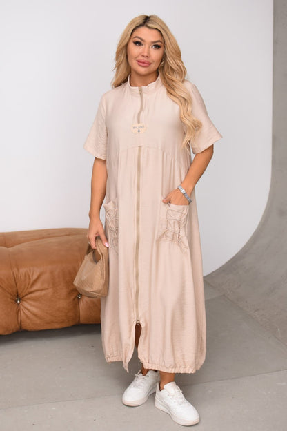 Woman wearing a beige dress with a brown leather couch in the background