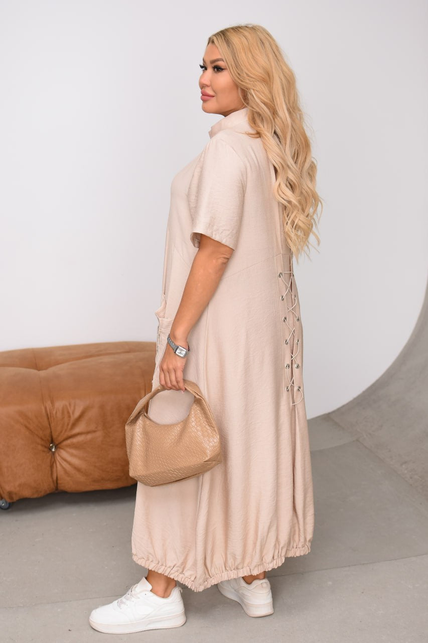 Woman in a long beige dress holding a matching handbag against a neutral background