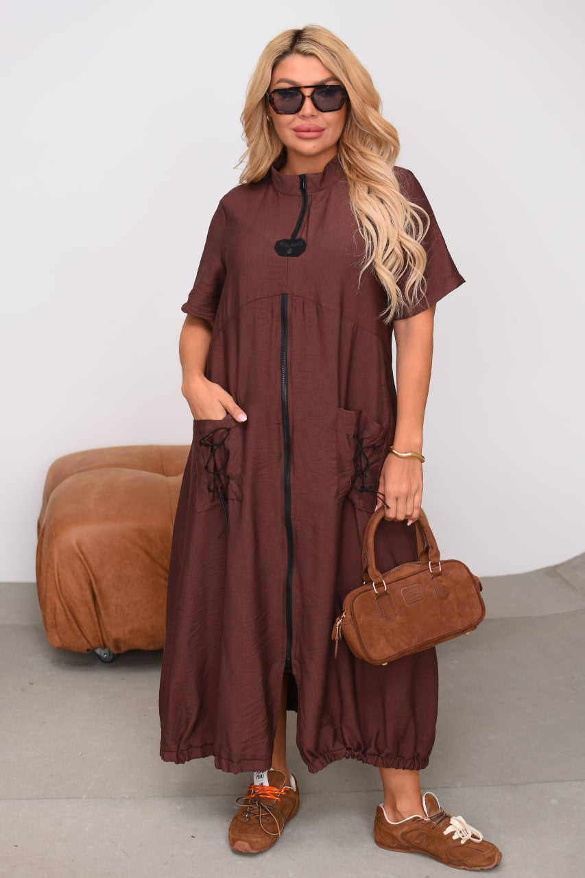Woman wearing a brown dress holding a matching handbag against a white background