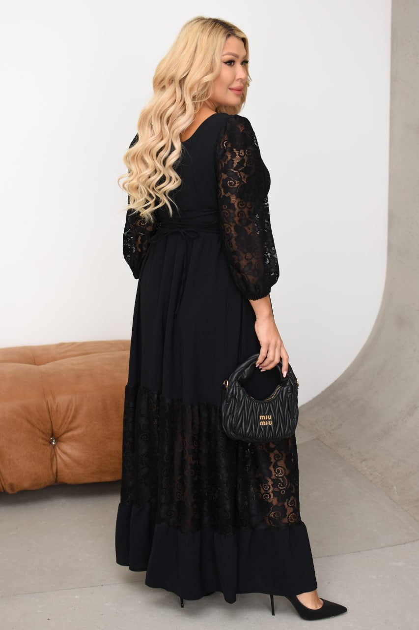 Woman wearing a black lace dress holding a matching handbag against a neutral background