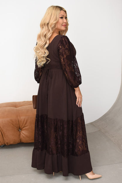 Woman wearing a long brown dress with lace details in a minimalistic setting.