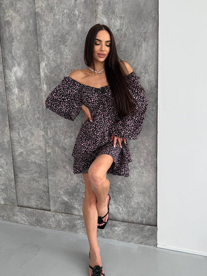 Woman wearing a floral off-shoulder dress against a gray wall.