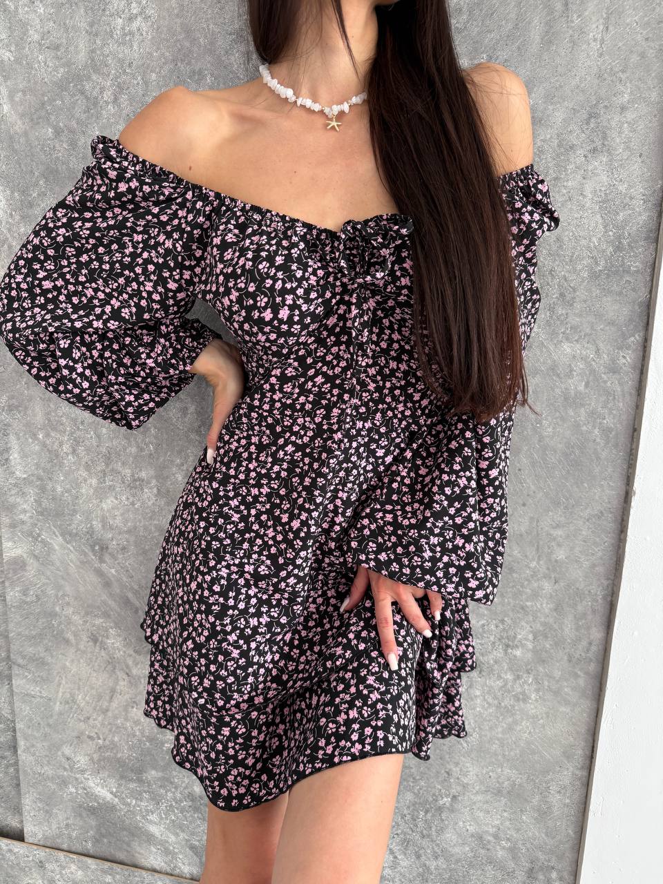 Woman wearing a black floral off-shoulder dress against a gray background