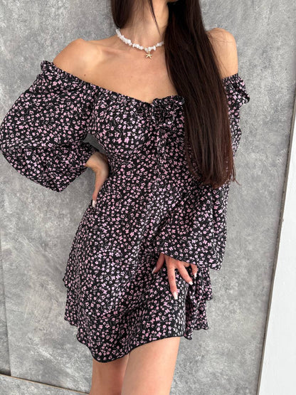 Woman wearing a black floral off-shoulder dress against a gray background