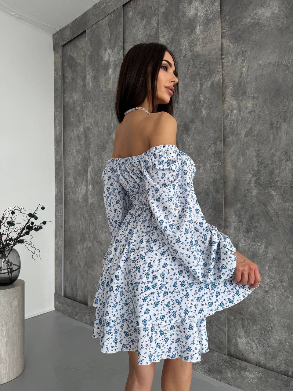 Woman wearing a white floral dress against a gray wall.