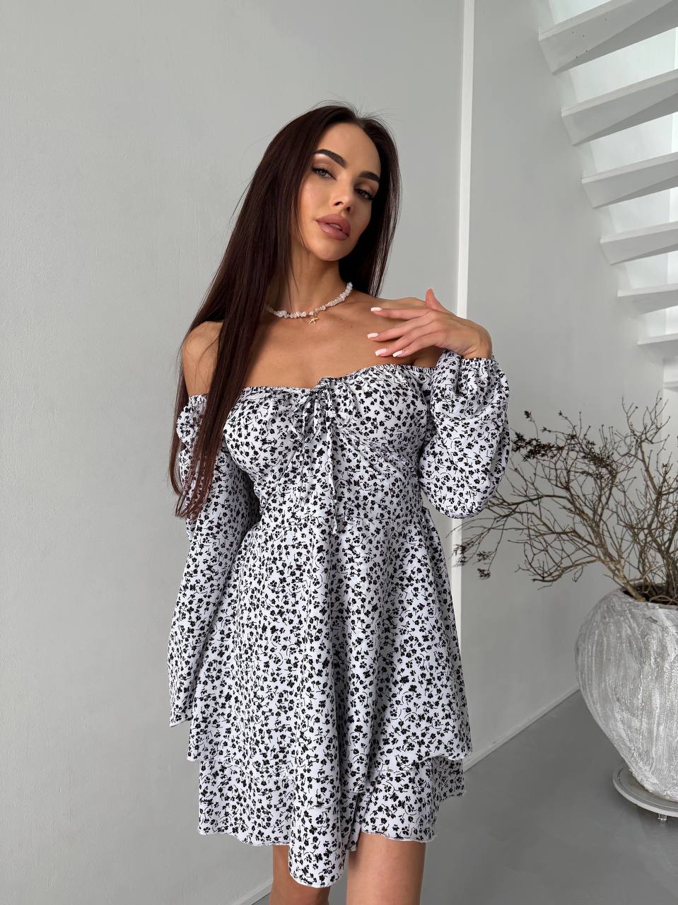 Woman wearing a black and white floral off-shoulder dress in a minimalistic room.