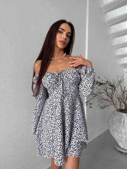 Woman wearing a black and white floral off-shoulder dress in a minimalistic room.