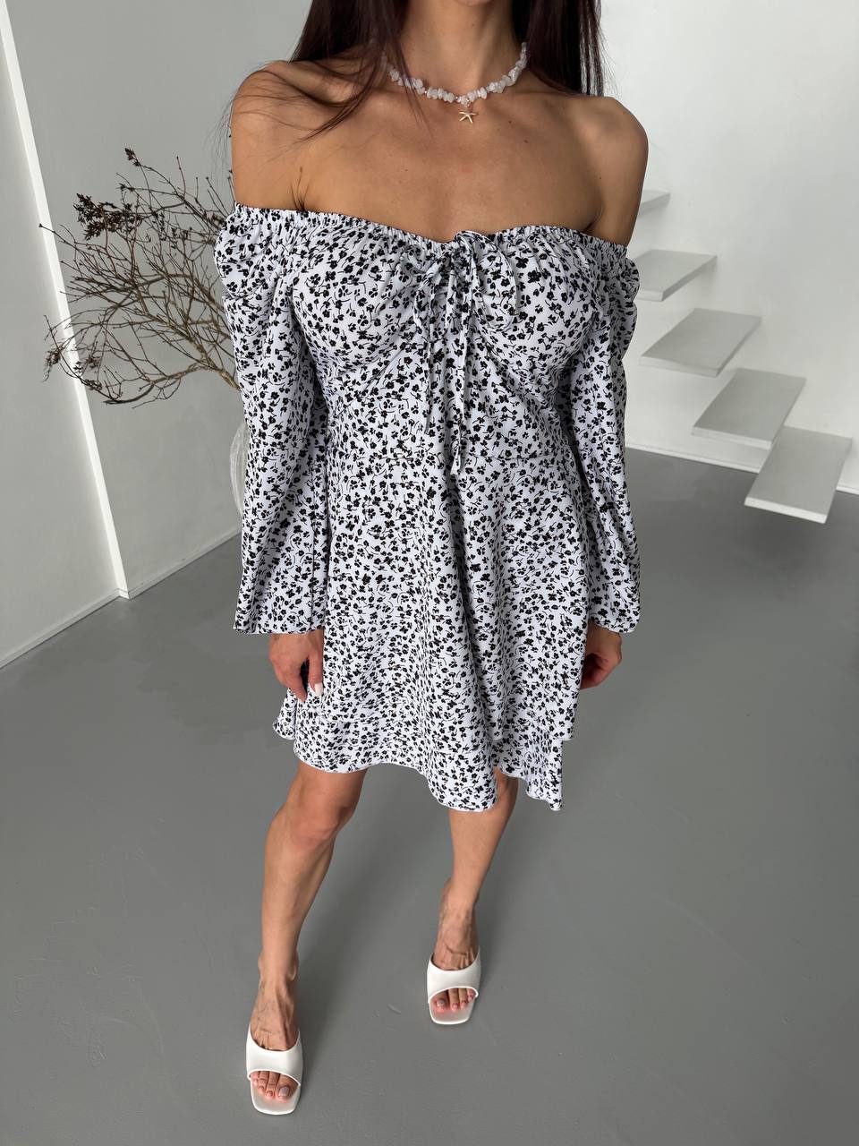 Woman wearing a black and white floral off-shoulder dress on a gray floor.