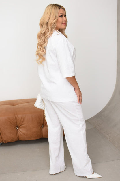 Woman wearing a white outfit standing in a minimalistic room with a brown sofa.