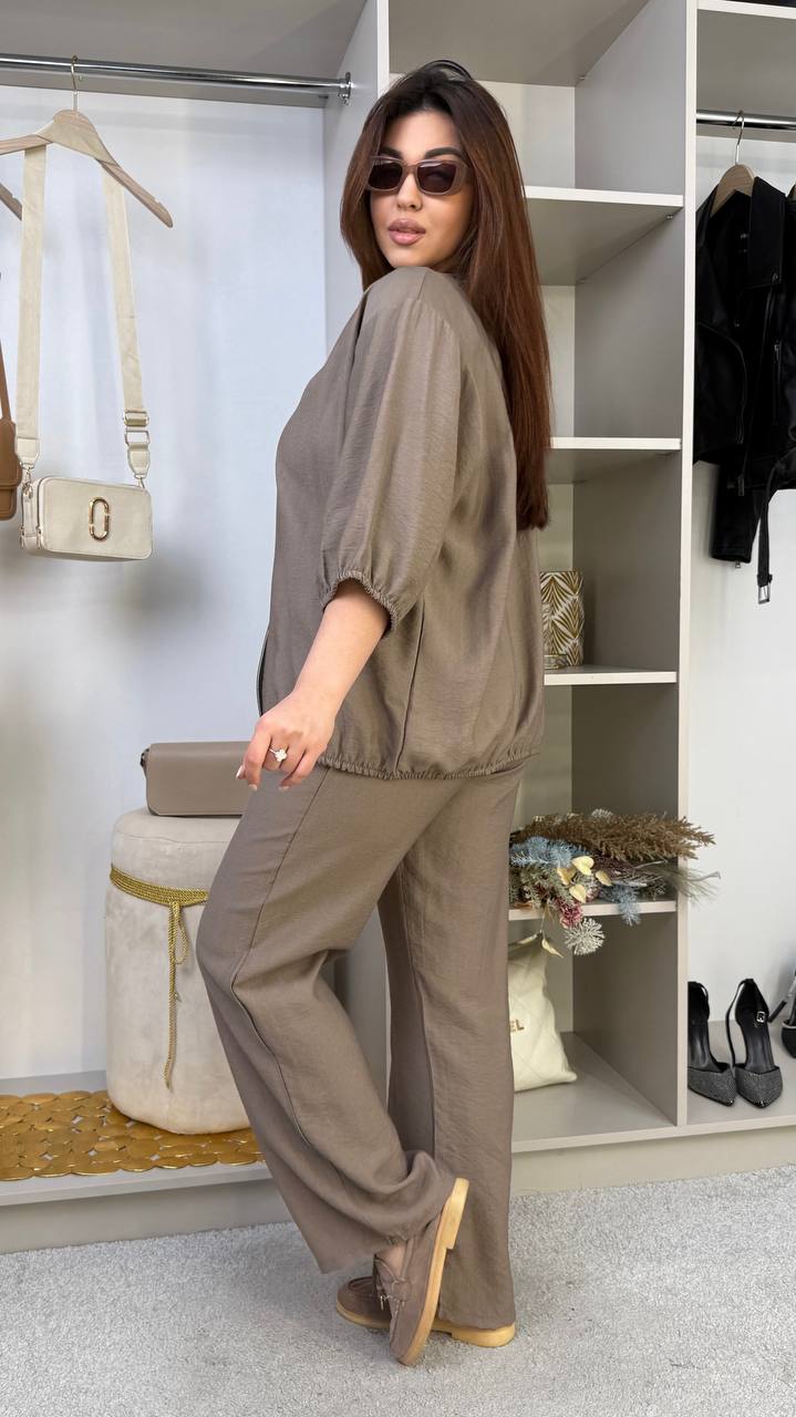Woman in a gray outfit standing in a room with shelves and clothing items.