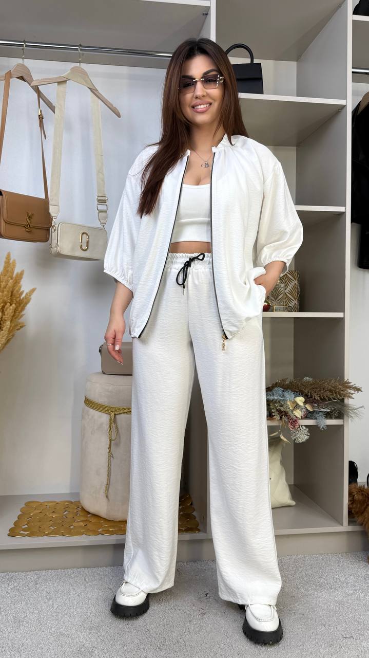 Woman in a white outfit standing in a room with shelves and decor.