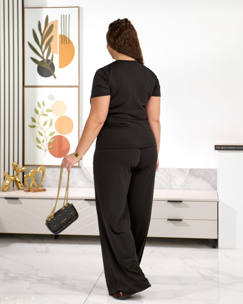 Woman in a black outfit standing in a room with decorative elements.