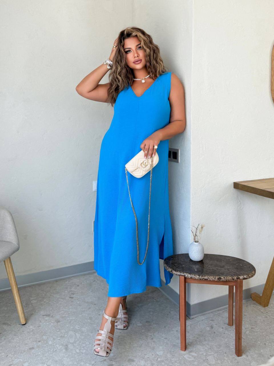 Woman in a blue dress standing indoors next to a small table.