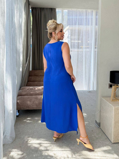 Woman in a blue dress standing in a room with curtains and a couch.