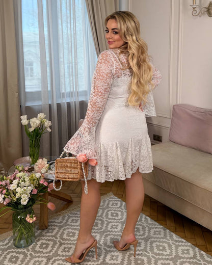 Woman in a white lace dress holding a woven handbag in a stylish room.
