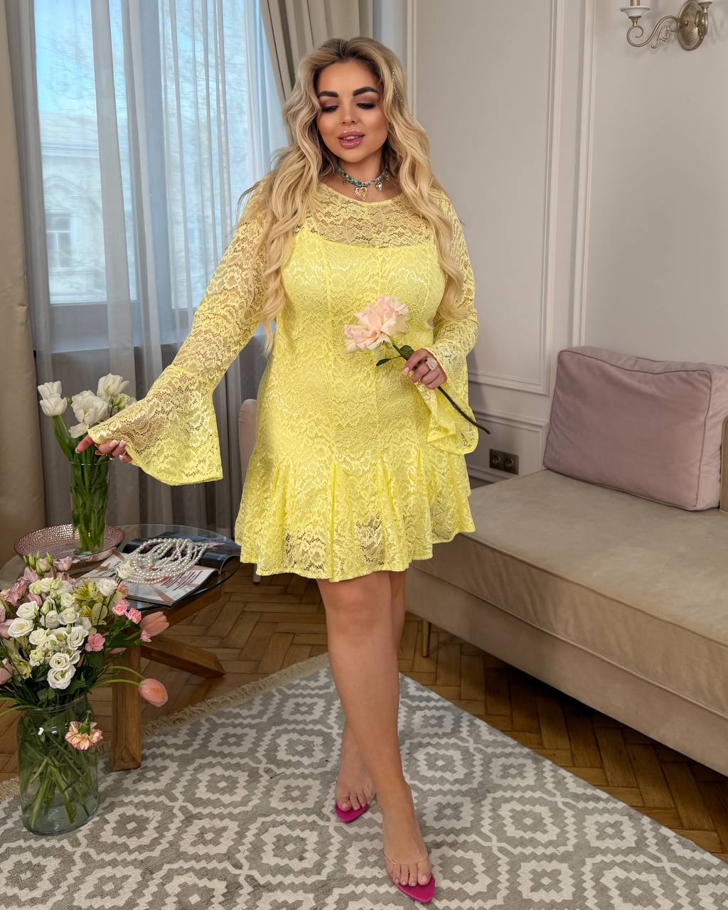 Woman in a yellow lace dress holding flowers in an elegant room.
