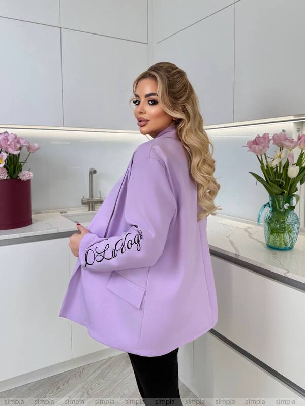 Woman wearing a light purple blazer with 'LOLA' branding in a kitchen setting.