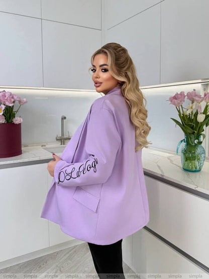 Woman wearing a light purple blazer with 'LOLA' branding in a kitchen setting.