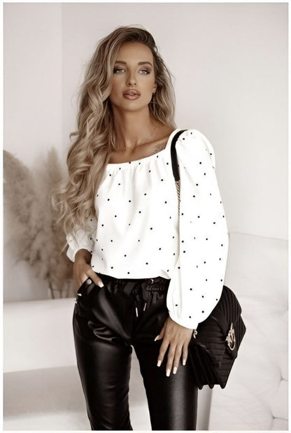 Woman wearing a white blouse with black polka dots and black leather pants, holding a black handbag.