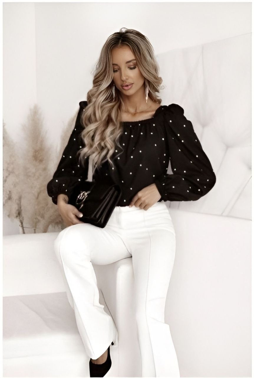 Woman wearing a black polka dot blouse and white pants sitting on a white couch.