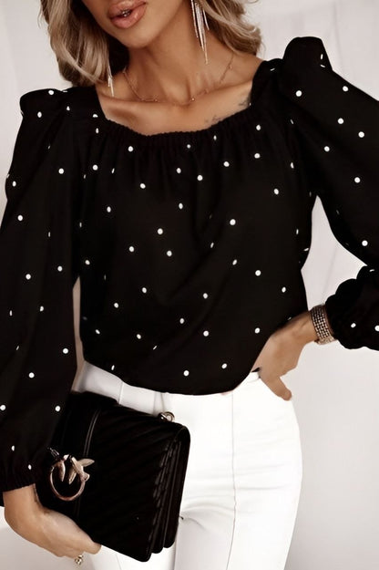 Woman wearing a black polka dot blouse holding a black clutch against a white background