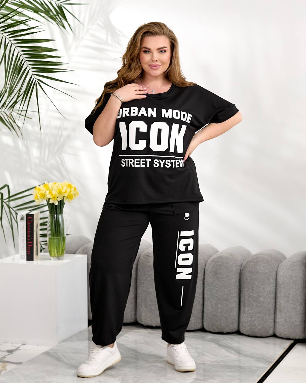 Woman wearing a black 'ICON' tracksuit in a living room setting