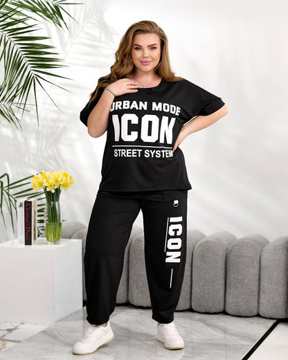 Woman wearing a black 'ICON' tracksuit in a living room setting