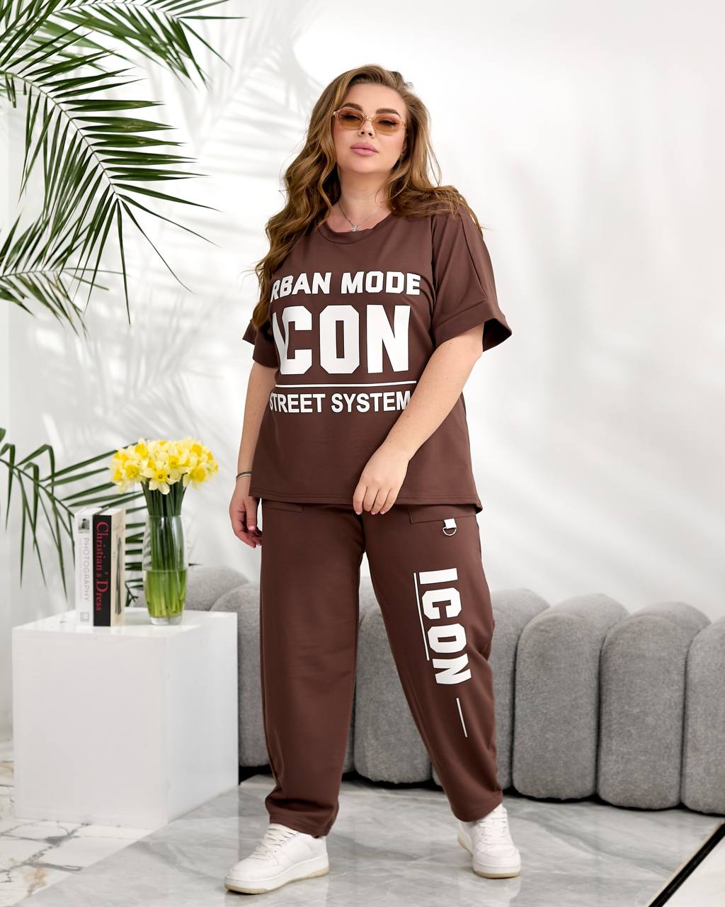 Woman wearing a brown 'ICON' outfit with text in a modern living room setting.