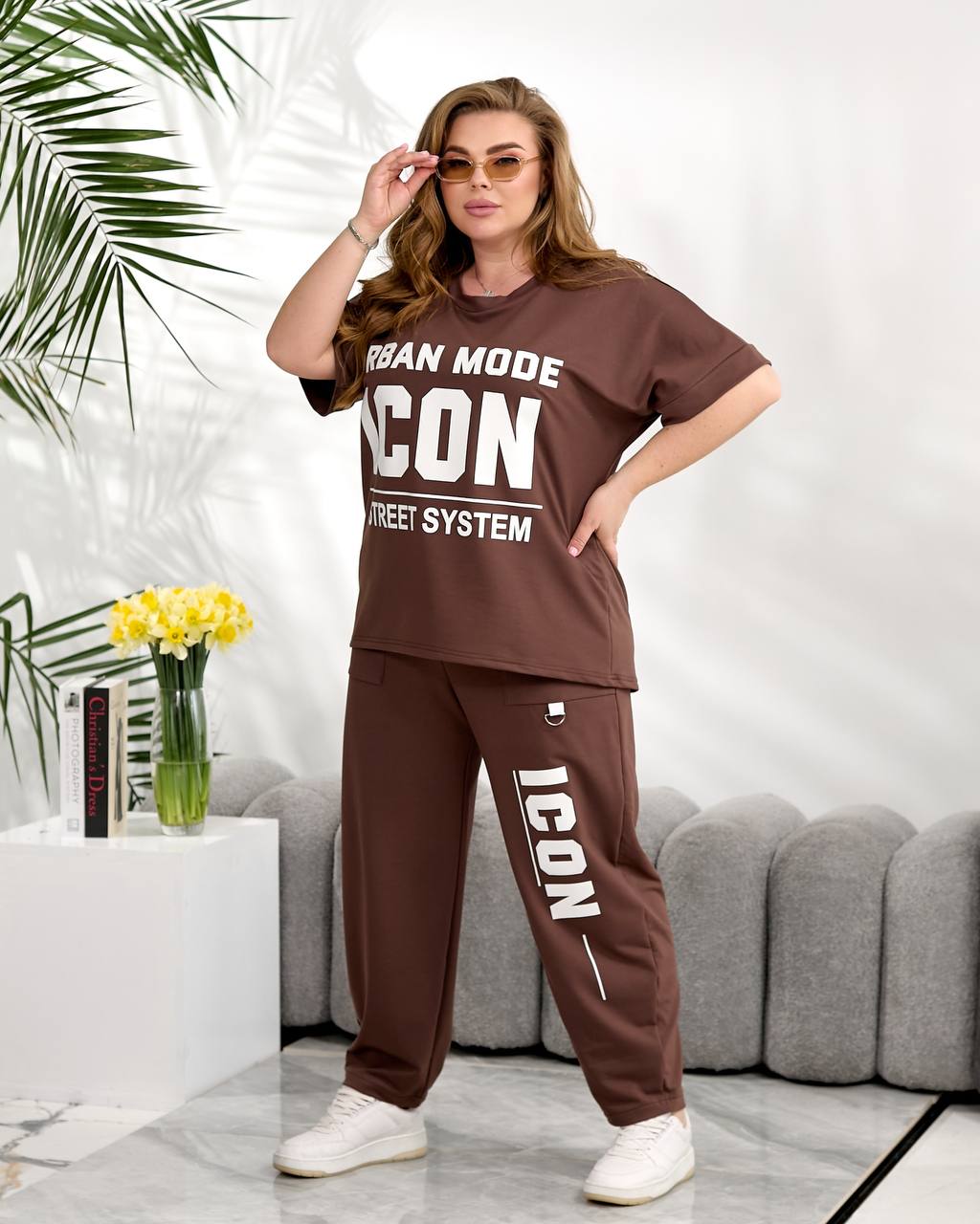 Woman wearing a brown 'ICON' tracksuit in a living room setting.